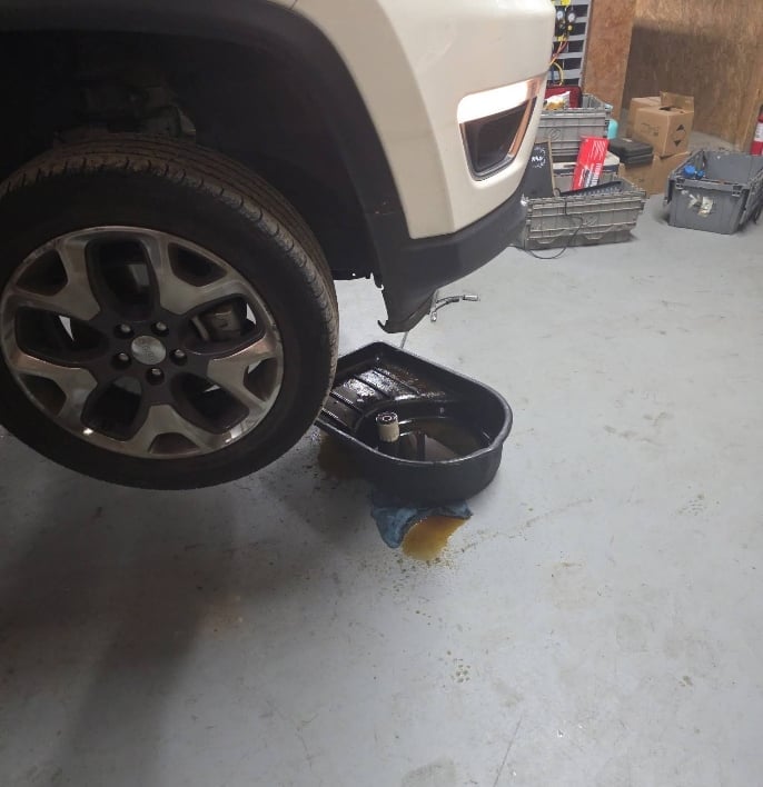 White vehicle tire and wheel positioned above a black oil drain pan on a concrete garage floor