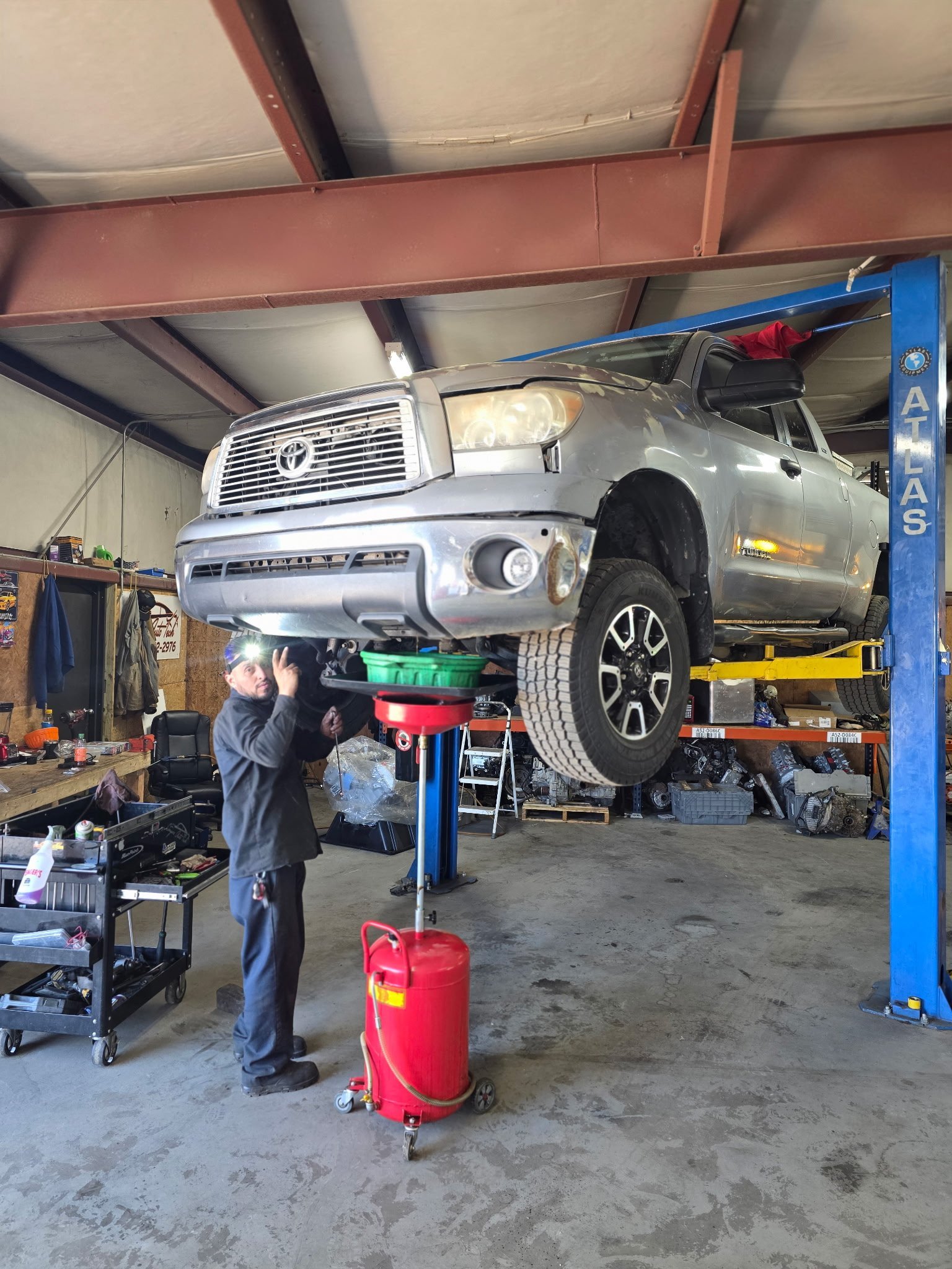 Mechanic working on a silver pickup truck lifted on a blue hydraulic lift in an auto repair shop garage