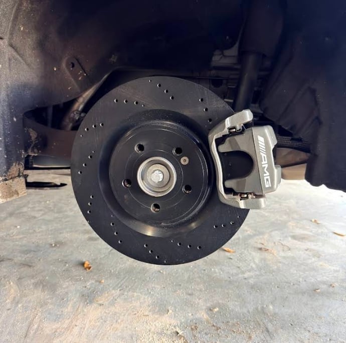 Black drilled brake rotor and caliper assembly on a vehicle wheel, close-up view